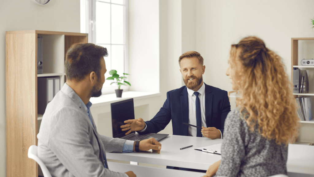 Three people sitting at a desk in a bright room talking